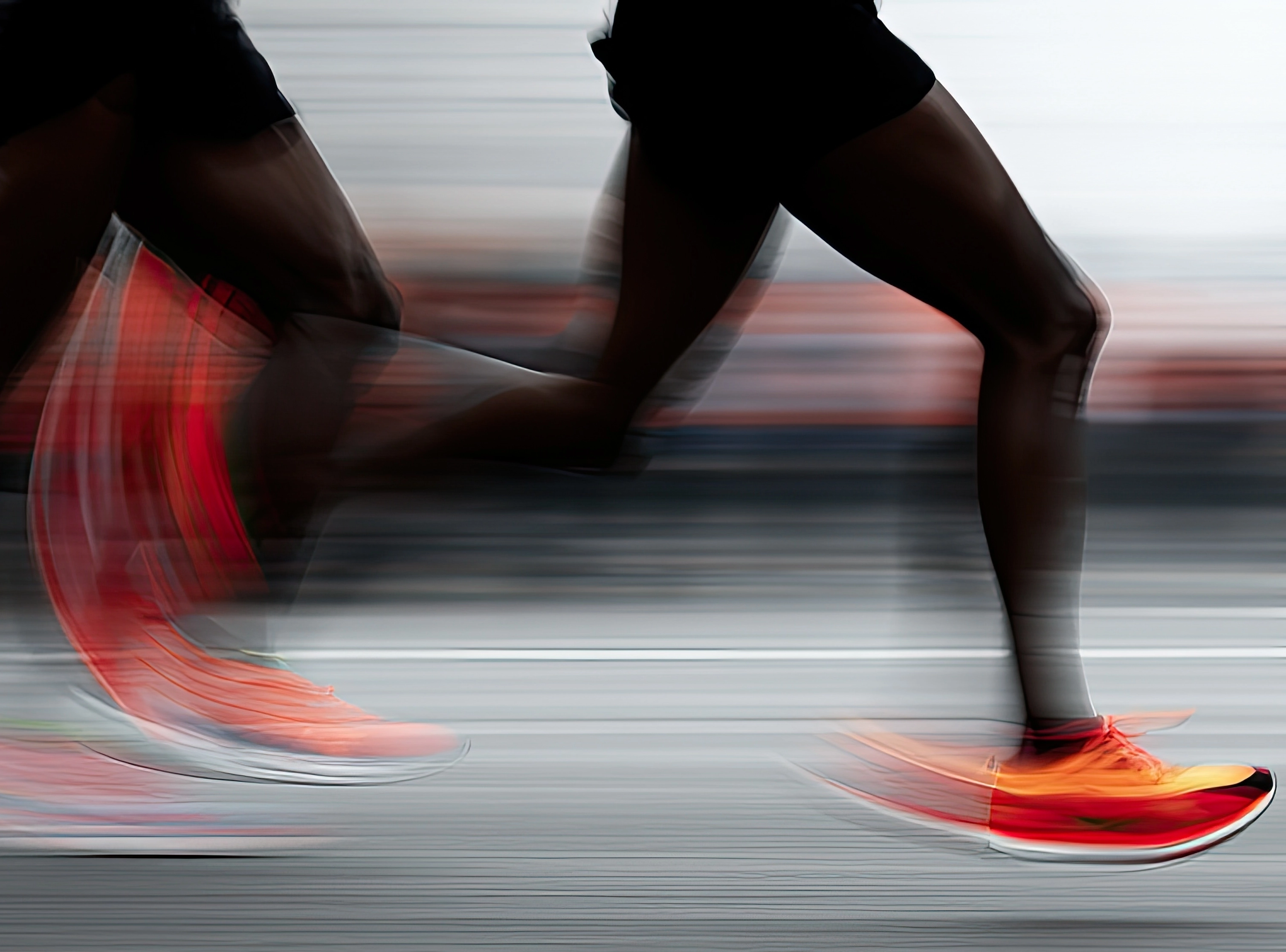 Two runners' legs in motion blur, wearing bright orange running shoes